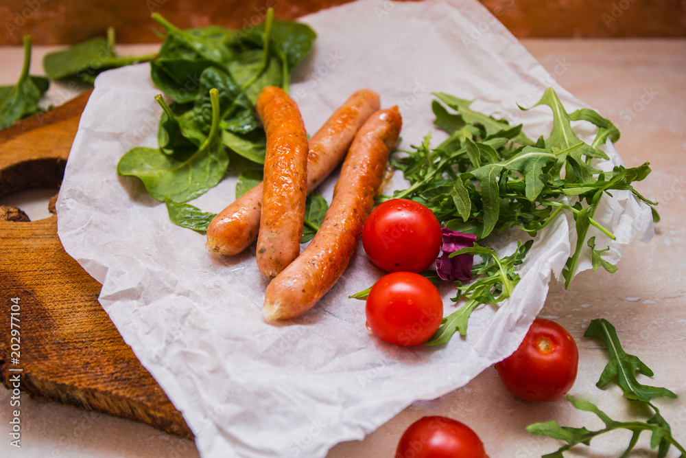 Grilled sausages with cherry tomatoes ,spinach and arugula on a wooden background in rustic style Grilled sausages with cherry tomatoes ,spinach and arugula on a wooden background in rustic style