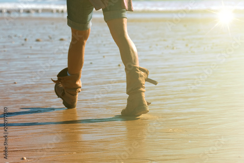 Woman in jeans shorts and summer boots walking on the sea water, along the coast. close-up of the legs and short 