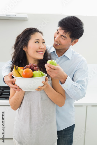 Young couple holding bowl full of fruit in kitchen