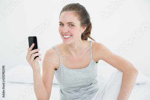 Smiling woman with mobile phone sitting in bed