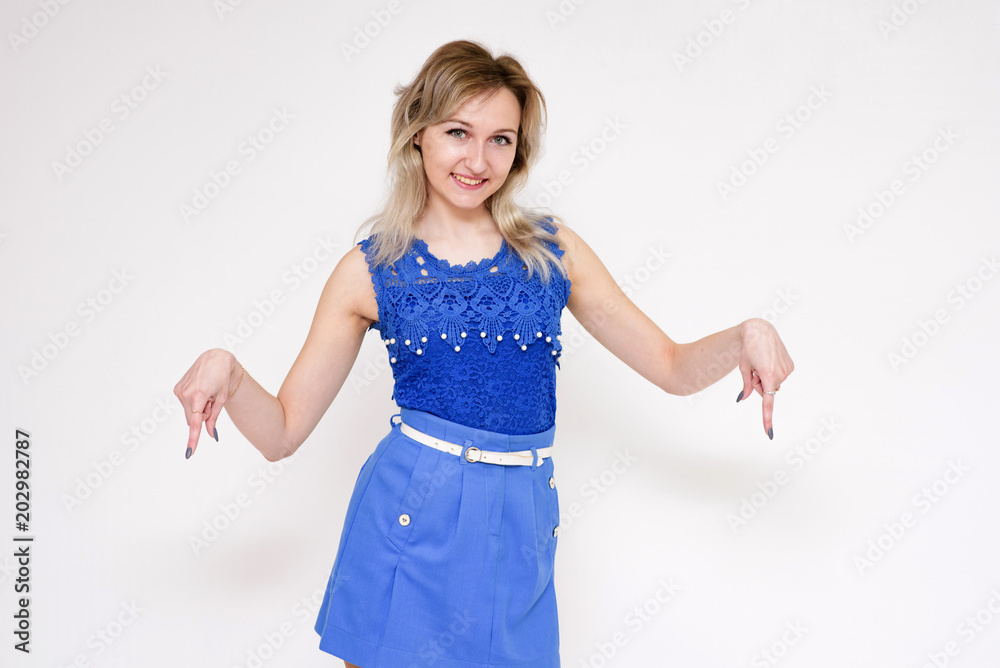 Look here - there is something interesting for you. Portrait of a beautiful blonde girl on a white background showing down. She is standing right in front of the camera and smiling Look here - there is something interesting for you. Portrait of a beautiful blonde girl on a white background showing down. She is standing right in front of the camera and smiling