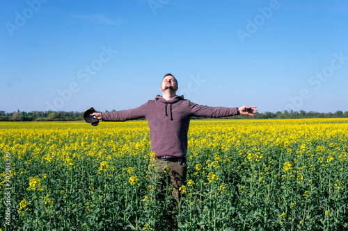 a man in a sweatshirt is standing in the field with arms spreading to the Field sown oilseed rape at the time of maximum spring flowering, biofuels. soil depletion from plants concept © Sergey