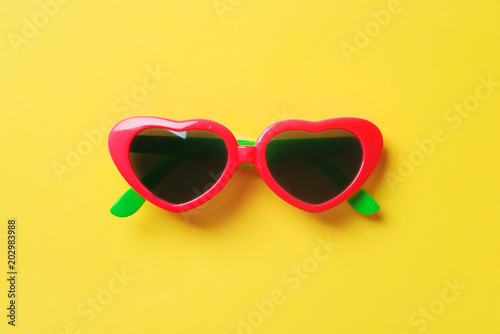 Cool red pink stylish woman sunglasses in a heart shape isolated on yellow pastel background, flat lay, top view. Fashion youth summer concept