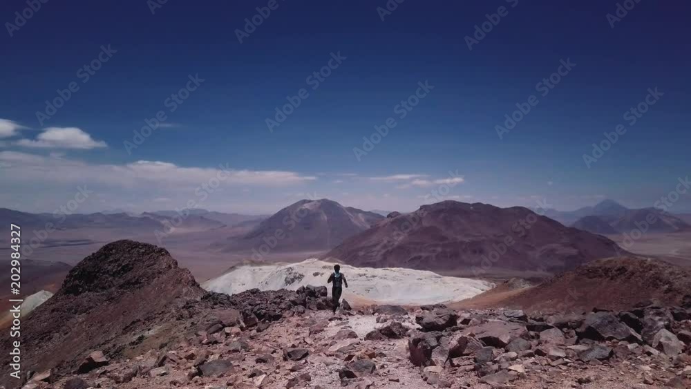 Male skyrunner achieving summit in a race on the mountain chain of the Atacama desert, 4k. Aerial footage of man ascending the summit of a mountain peak. Male skyrunner achieving summit in a race on the mountain chain of the Atacama desert, 4k. Aerial footage of man ascending the summit of a mountain peak.