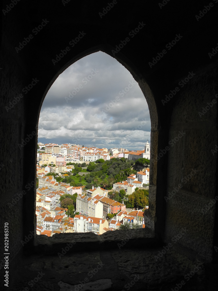 Bright city view with red roofs and beautiful cloudy sky through arched window in old stone wall, Lisbon, Portugal