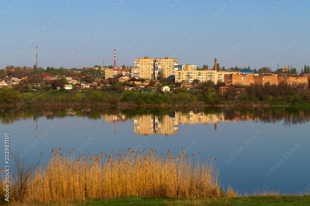Reflection of multi-storey buildings in the calm and flat surface of the lake in the early morning.
