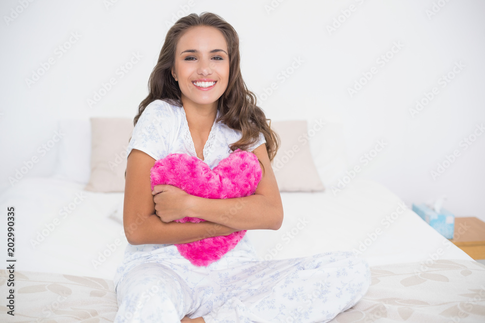 Happy attractive brunette holding a heart pillow Happy attractive brunette holding a heart pillow