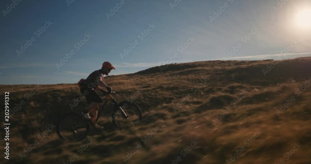 Tracking shot of fast mountain biker riding up the hill in amazing sun. Tracking shot of fast mountain biker riding up the hill in amazing sun.