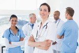 Confident female doctor smiling at camera with her team behind