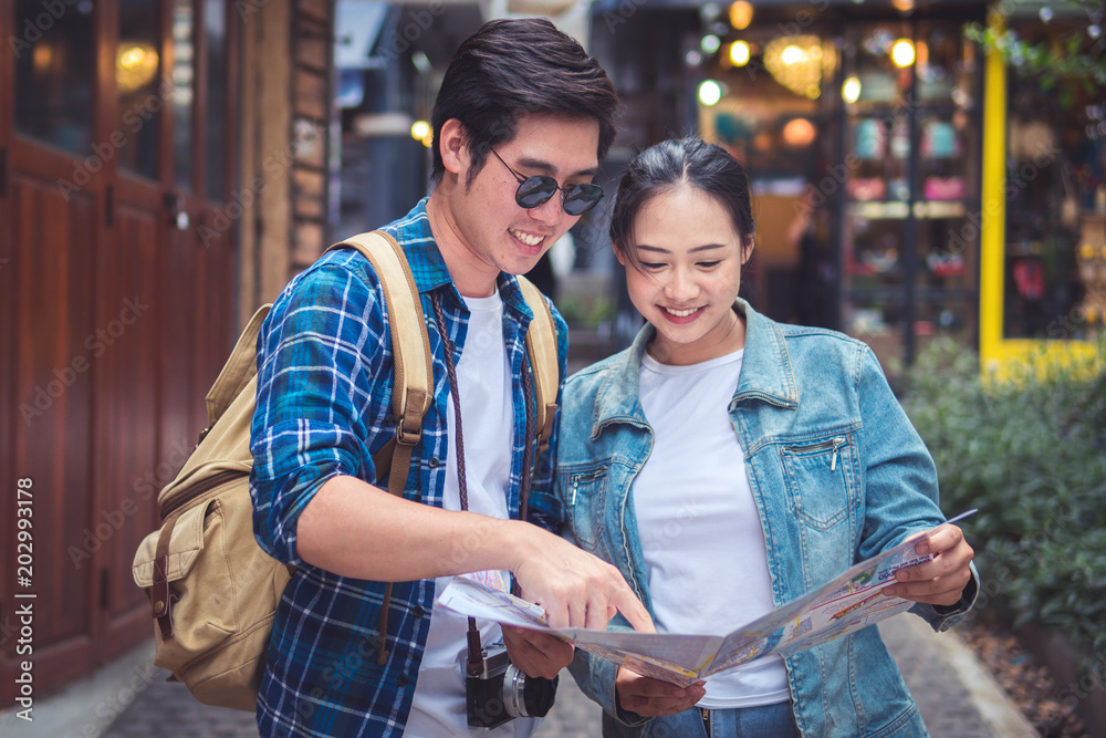 Couple Of Travelers Using Map For Sightseeing In Town. Portrait Of Young Smiling Tourist Man And Woman Holding Map In Hands, Walking On Street And Traveling Together. High Resolution.