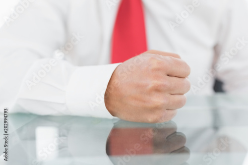 Mid section of a businessman with clenched fist on desk