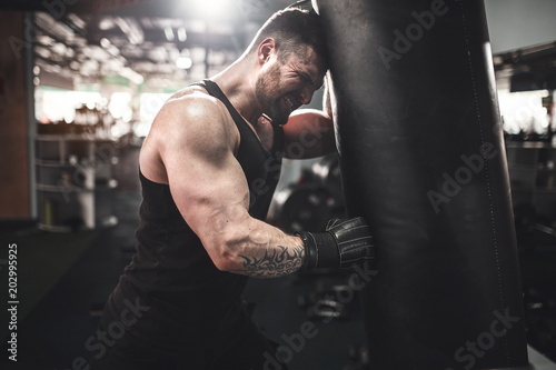 фотографія Bearded Male boxer training with punching bag in dark sports hall