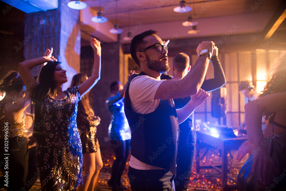 Fotografie Crowd of trendy  people dancing in nightclub with golden confetti flying around,