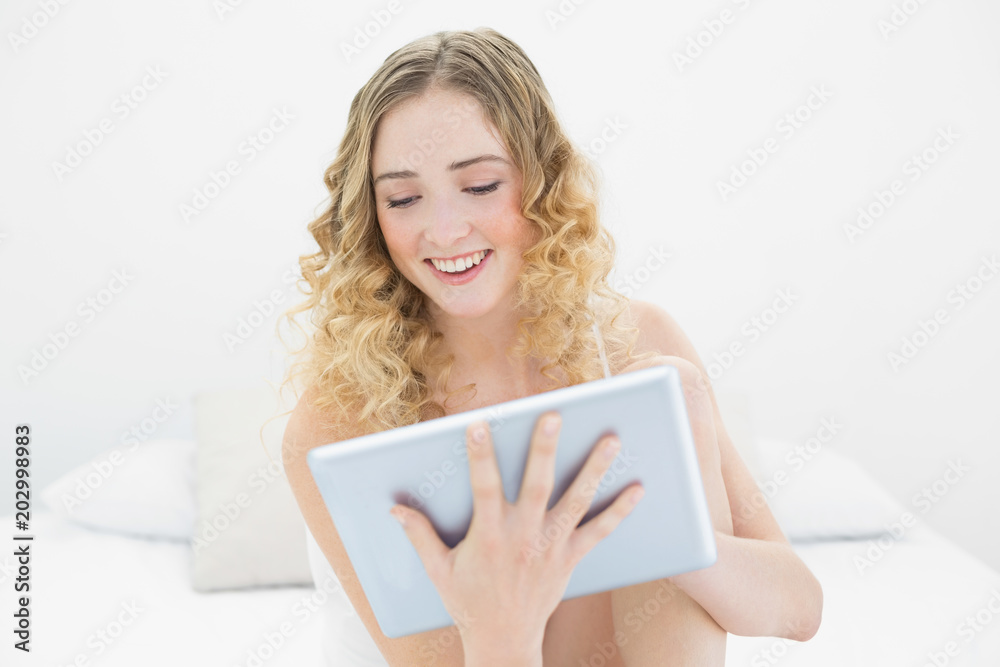 Pretty smiling blonde sitting on bed using tablet Pretty smiling blonde sitting on bed using tablet