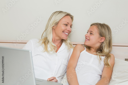Relaxed mother and daughter with laptop in bed