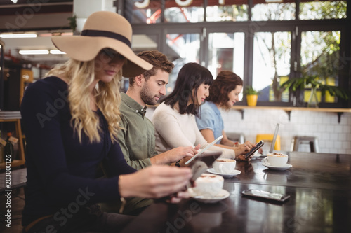 Friends using mobile phones while sitting with coffee cups in cafe