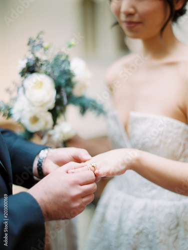 Close-up of bridegroom placing ring on finger of bride at wedding