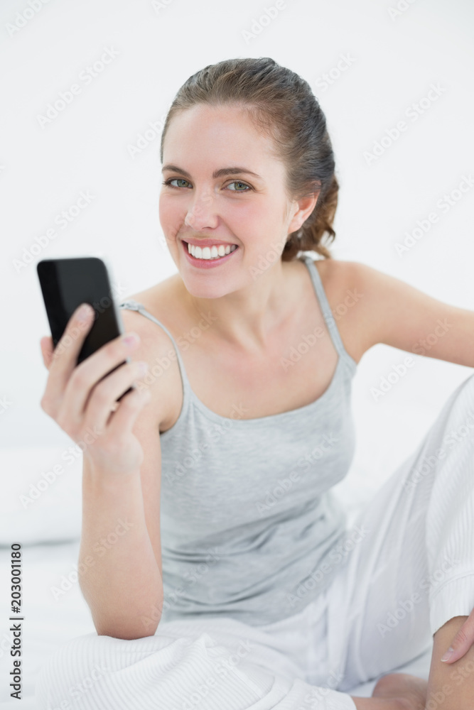 Smiling woman with mobile phone sitting in bed