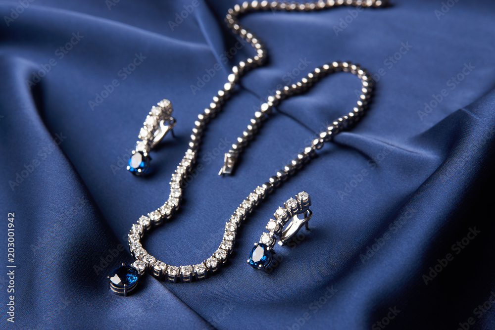 Fototapeta premium Close-up of women's platinum necklace and earrings with a diamond and blue precious sapphire stone . Luxury female jewelry