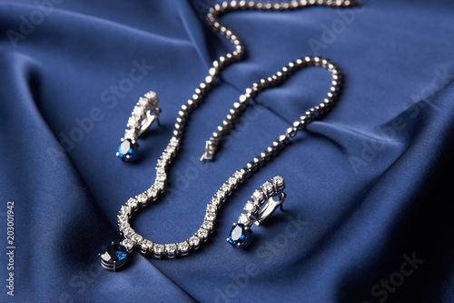 Close-up of women's platinum necklace and earrings with a diamond and blue precious sapphire stone . Luxury female jewelry