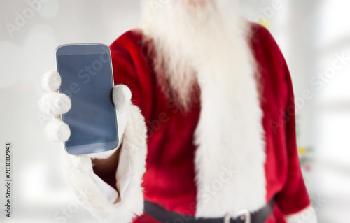 Santa claus showing smartphone against blurry christmas tree in room