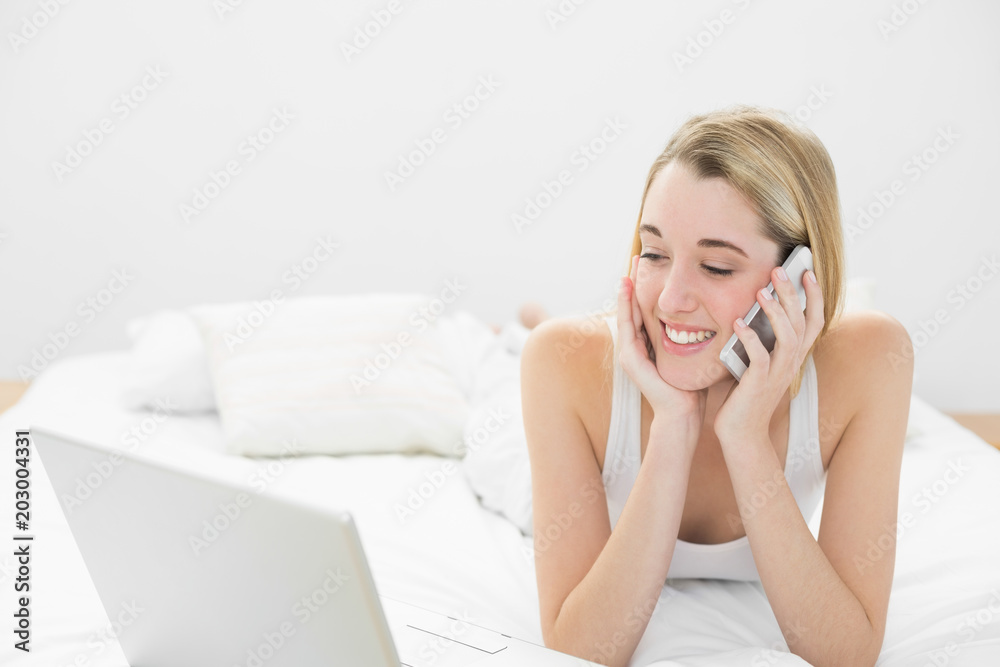 Beautiful woman phoning while lying on her bed using her notebook Beautiful woman phoning while lying on her bed using her notebook