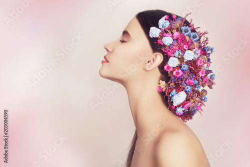 Fototapeta Naklejka Na Ścianę i Meble -  Beautiful young woman with delicate flowers in their hair. Beauty Girl with Flowers Hairstyle.Model portrait with Summer pink and blue Flowers. Hairstyle with flowers. Fantasy portrait in pink. Smile.