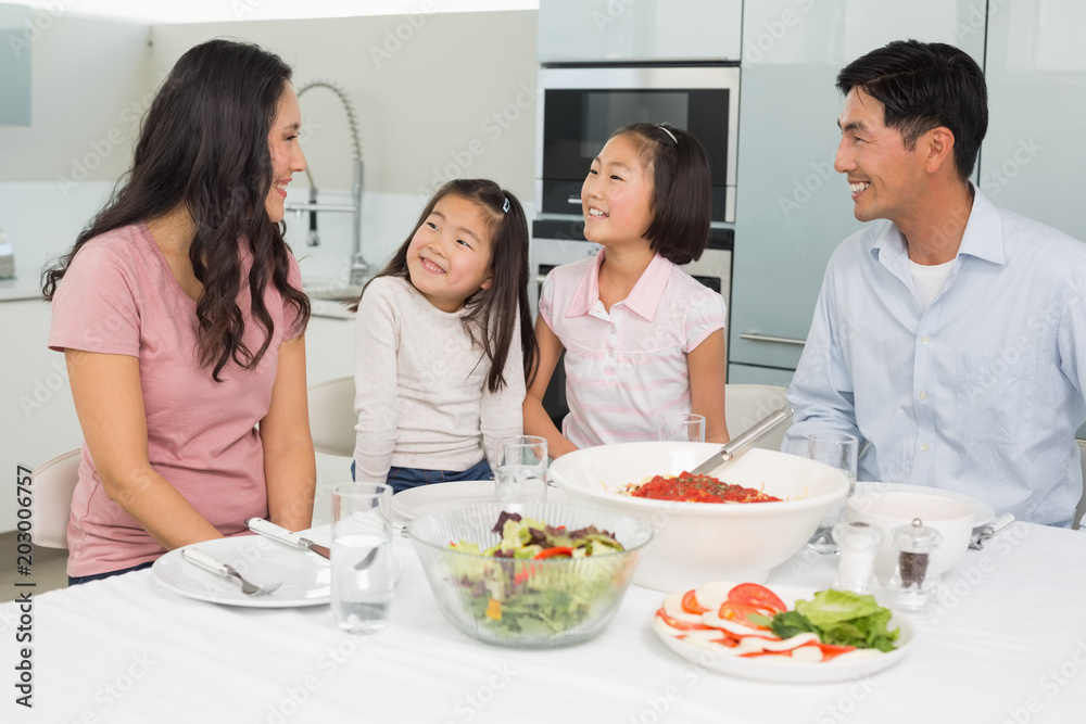 Smiling family of four sitting at dining table in kitchen Smiling family of four sitting at dining table in kitchen