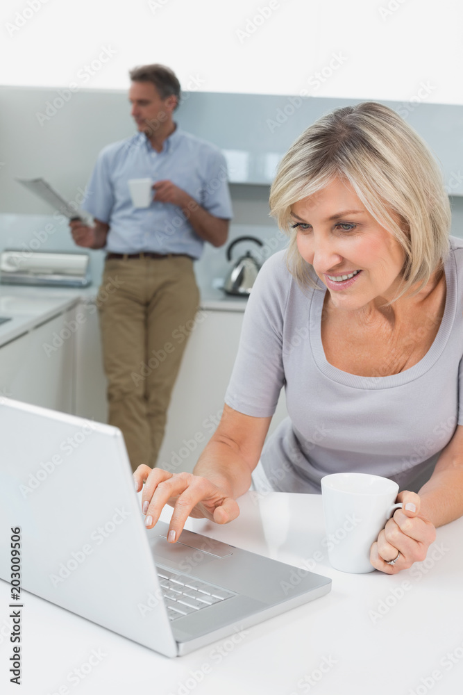 Woman using laptop and man reading newspaper in kitchen Woman using laptop and man reading newspaper in kitchen