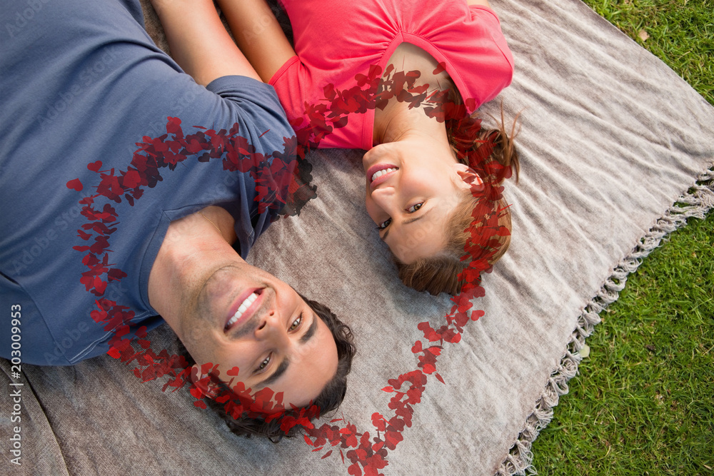 Two friends looking towards the sky while lying on a quilt against heart made of petals
