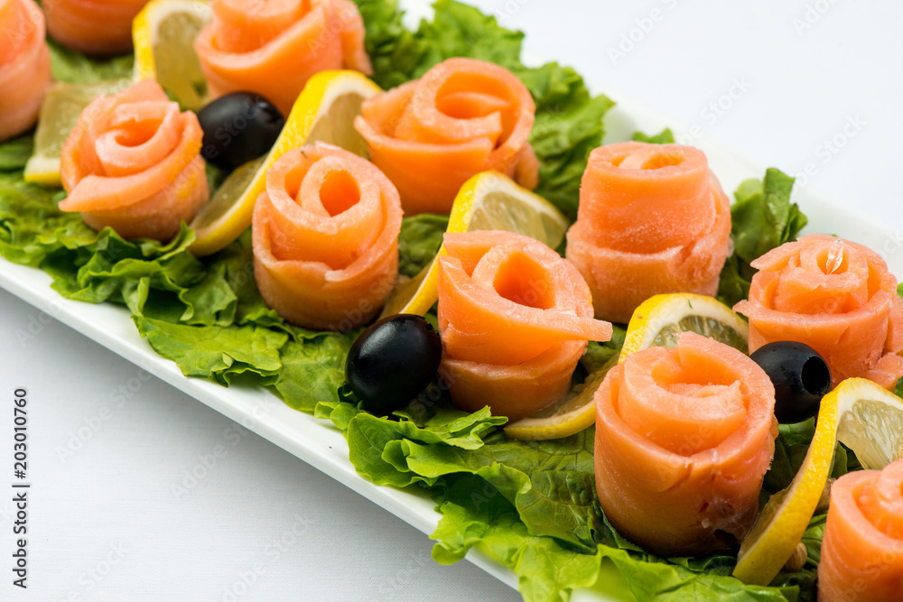 salmon snack on lettuce leaf with lemon and olives on white plate on white background salmon snack on lettuce leaf with lemon and olives on white plate on white background