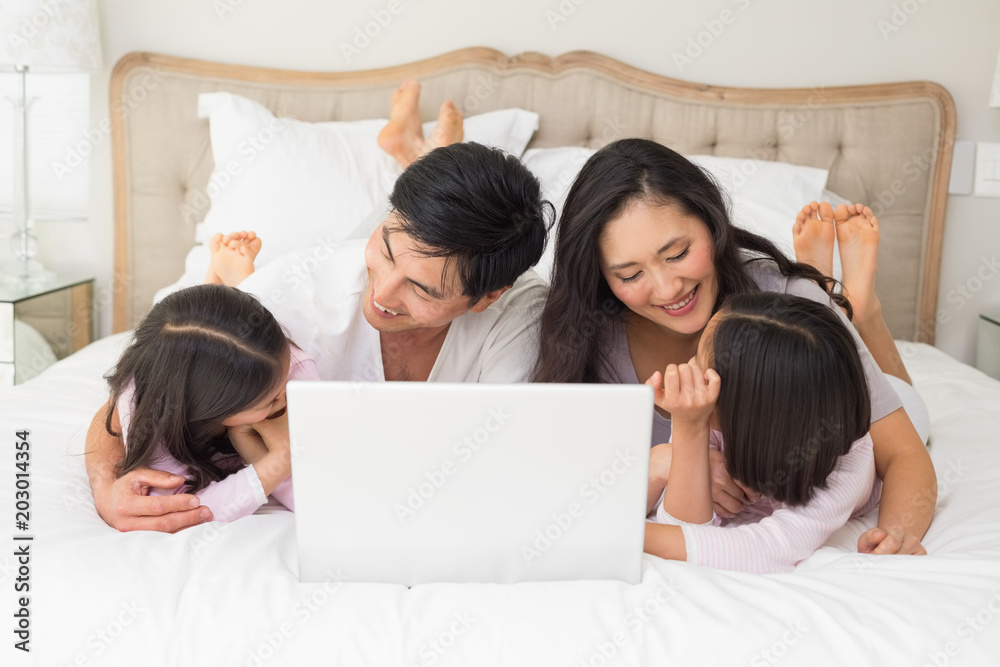 Happy family of four using laptop in bed Happy family of four using laptop in bed