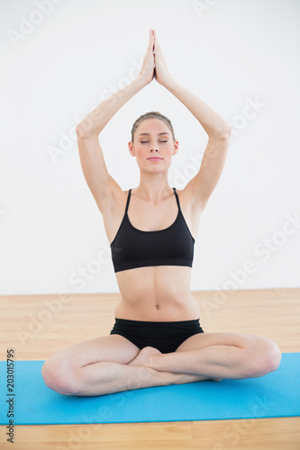 Calm slender woman sitting in lotus position on blue exercise mat 