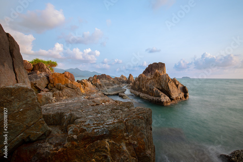 Large rocks and spiky filed in sea green waters and golden evening sky. Long Exposure Photography Technique .Chai Chet, Koh Chang, Trat, Thailand © Suwun