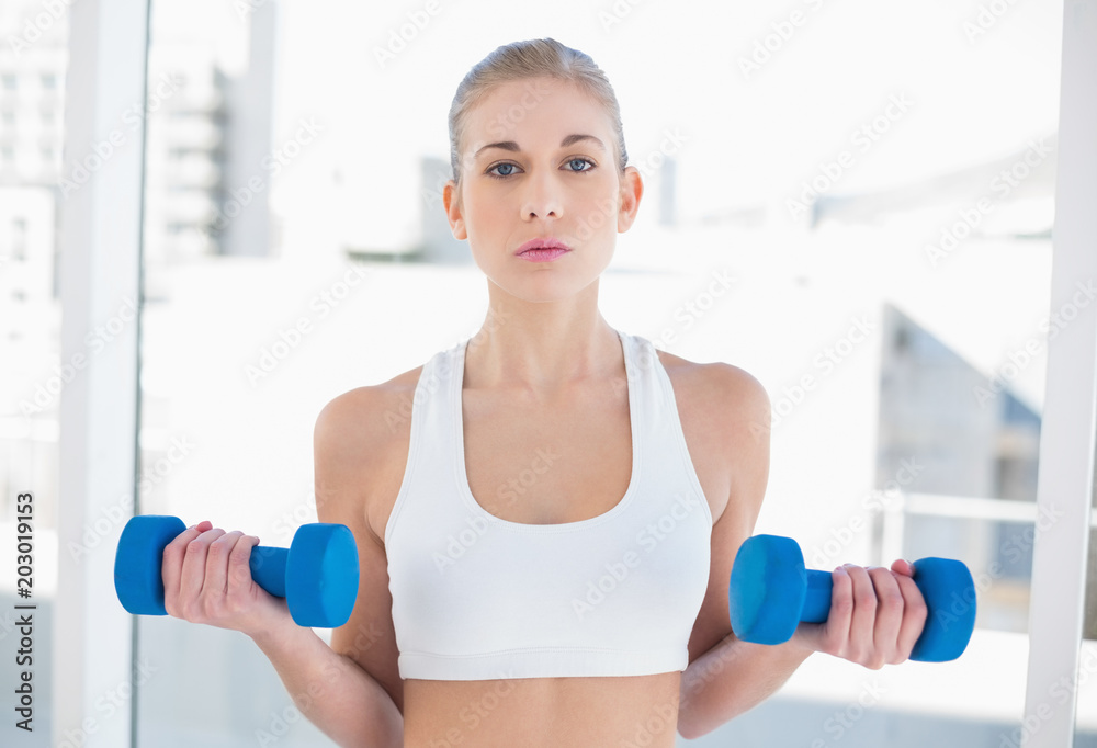 Attentive young blonde model exercising with dumbbells