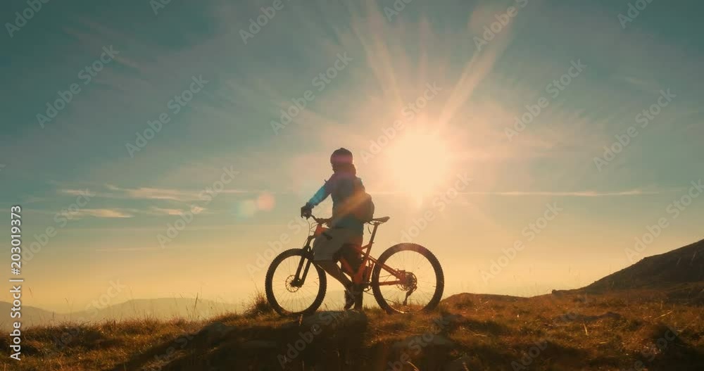 Mountain biker reaching the top celebrating with lifting his bike to the sky in amazing evening light.