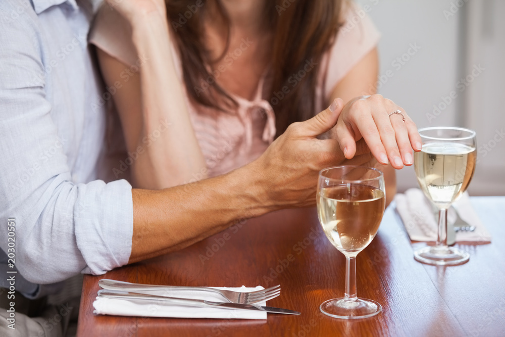 Mid section of woman showing engagement ring with wine glasses on table
