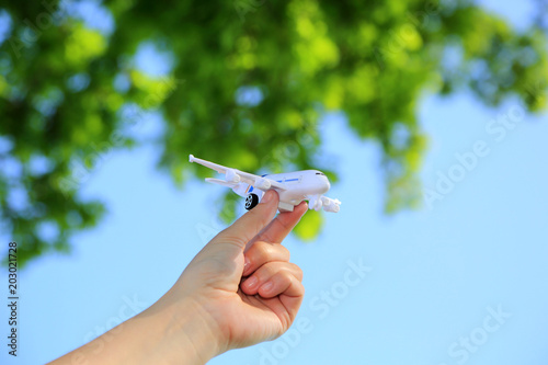 Samolot zabawka w dłoni dziewczyny na tle błękitnego nieba i zielonych liści.