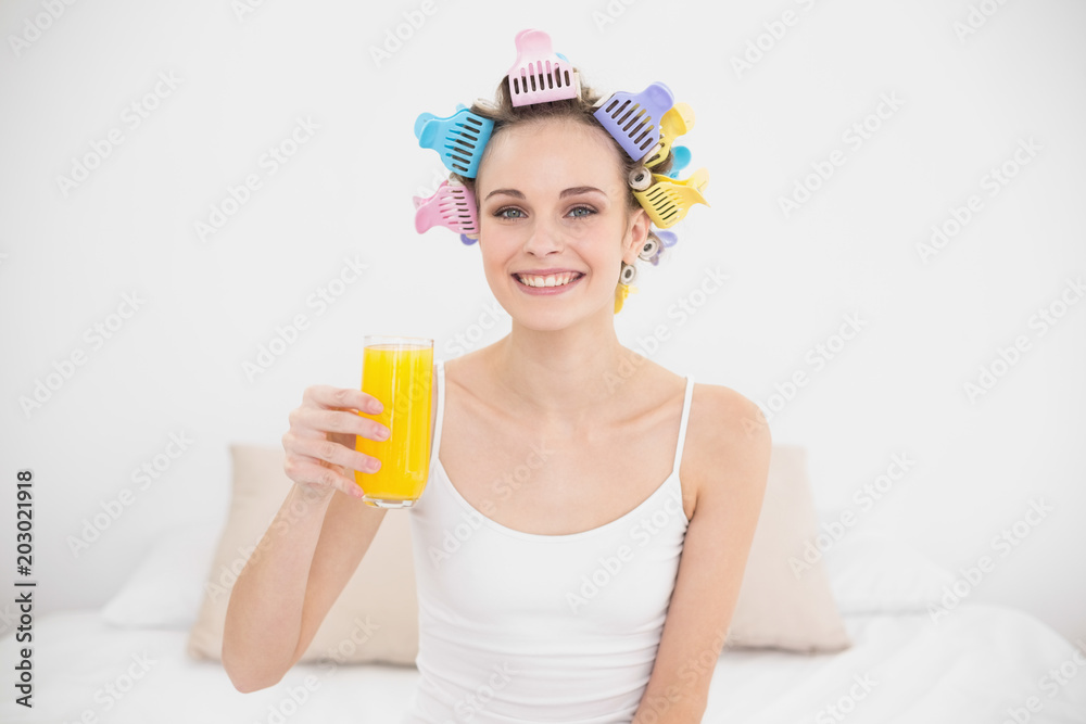 Charming natural brown haired woman in hair curlers holding a glass of orange juice Charming natural brown haired woman in hair curlers holding a glass of orange juice