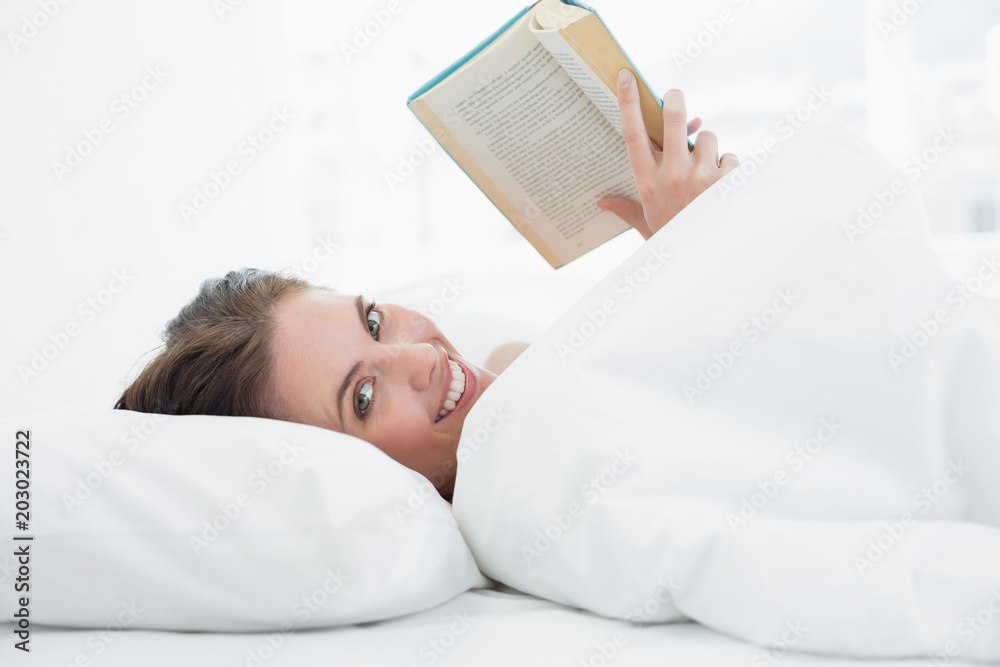 Smiling young woman reading a book in bed Smiling young woman reading a book in bed