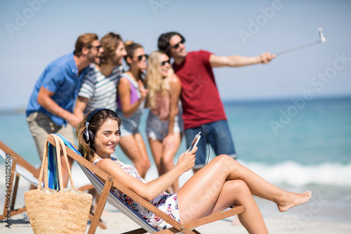 Woman listening music while friends taking selfie at beach © WavebreakmediaMicro