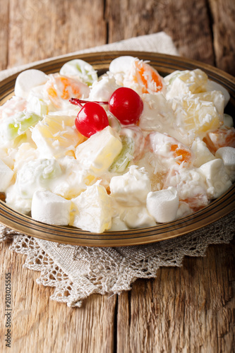 Delicious salad Ambrosia made from pineapple, tangerine, grapes and marshmelou with vanilla yogurt close-up on a plate. vertical