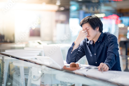 Young Asian business man feeling stressed and frustrated while working with laptop computer. Male entrepreneur getting in trouble with his job. freelance lifestyle in urban workspace. photo