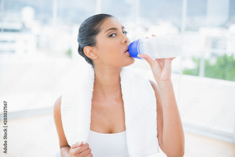 Calm toned brunette with towel drinking from sports bottle Calm toned brunette with towel drinking from sports bottle