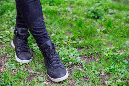 woman legs in black jeans and black shoes on green grass background. copy space