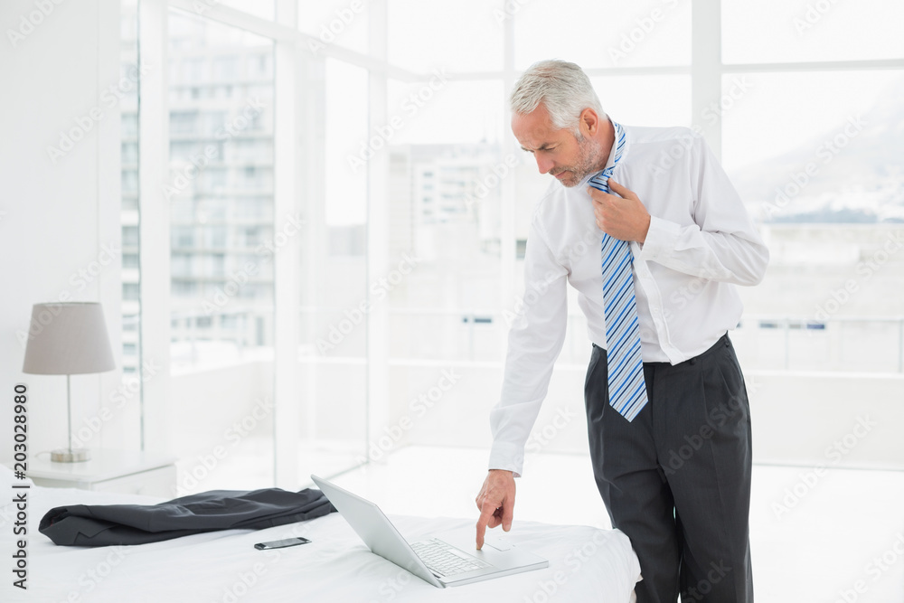 Businessman wearing tie while using laptop at a hotel room Businessman wearing tie while using laptop at a hotel room
