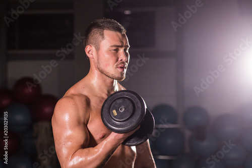 Handsome power athletic man with dumbbell. Strong bodybuilder with six pack, perfect abs, shoulders, biceps, triceps and chest
