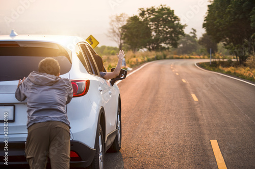 Man pushing a broken car down the road