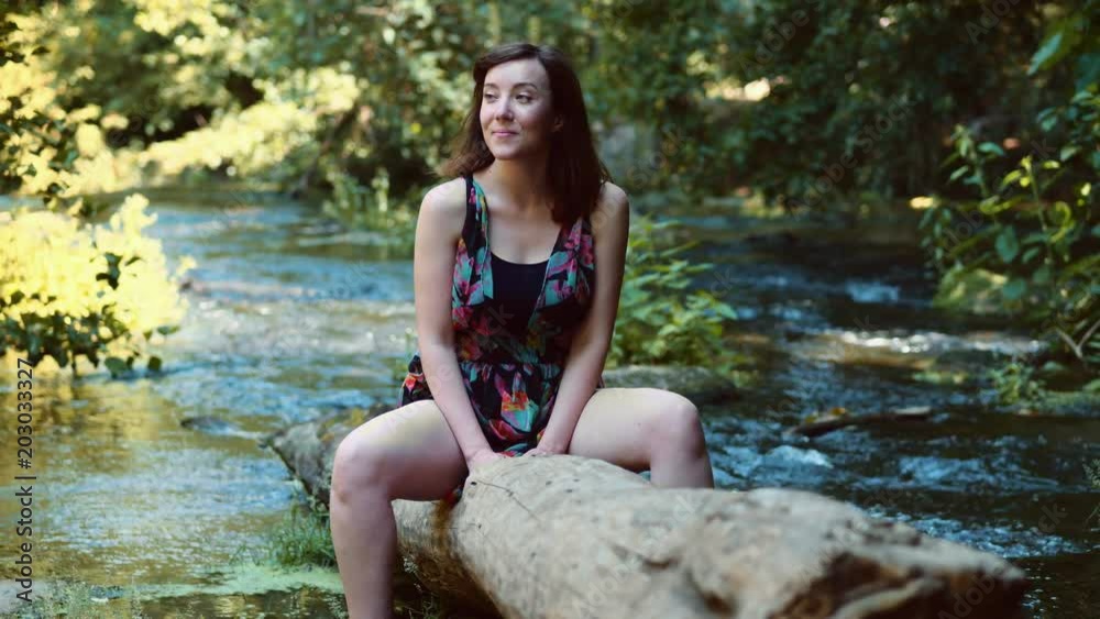 relaxed pretty caucasian woman sit on tree trunk in the river relaxed pretty caucasian woman sit on tree trunk in the river