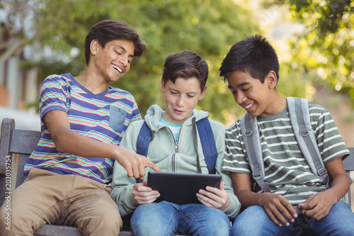 School kids using digital tablet on bench